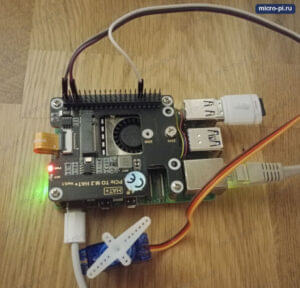 Сервопривод SG90 с белой качалкой подключён тремя проводами к контактам GPIO Raspberry Pi 5, сверху на плате стоит M.2 HAT+